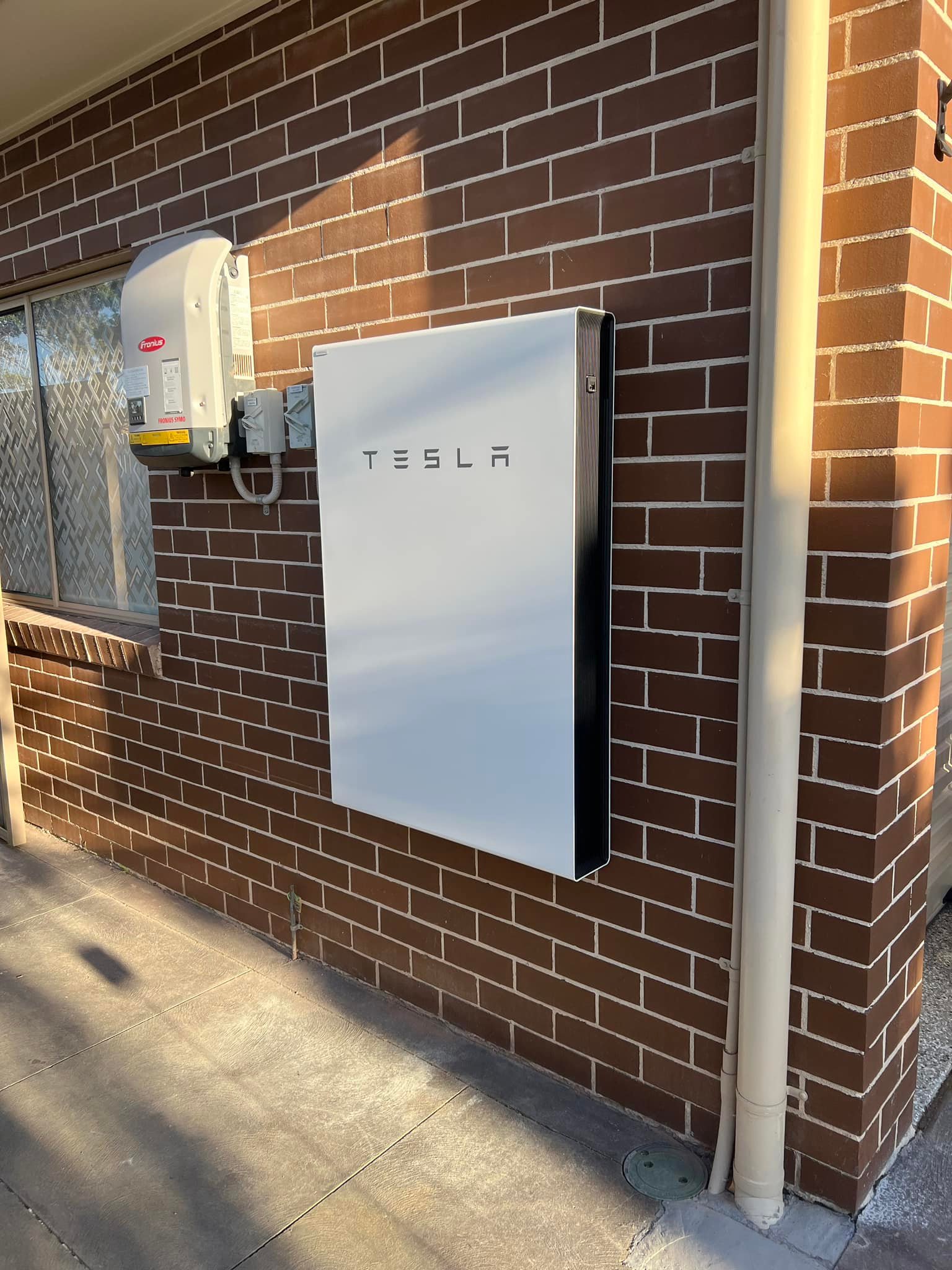 Tesla Powerwall home battery mounted on an exterior brick wall, installed by Clean Earth Solar